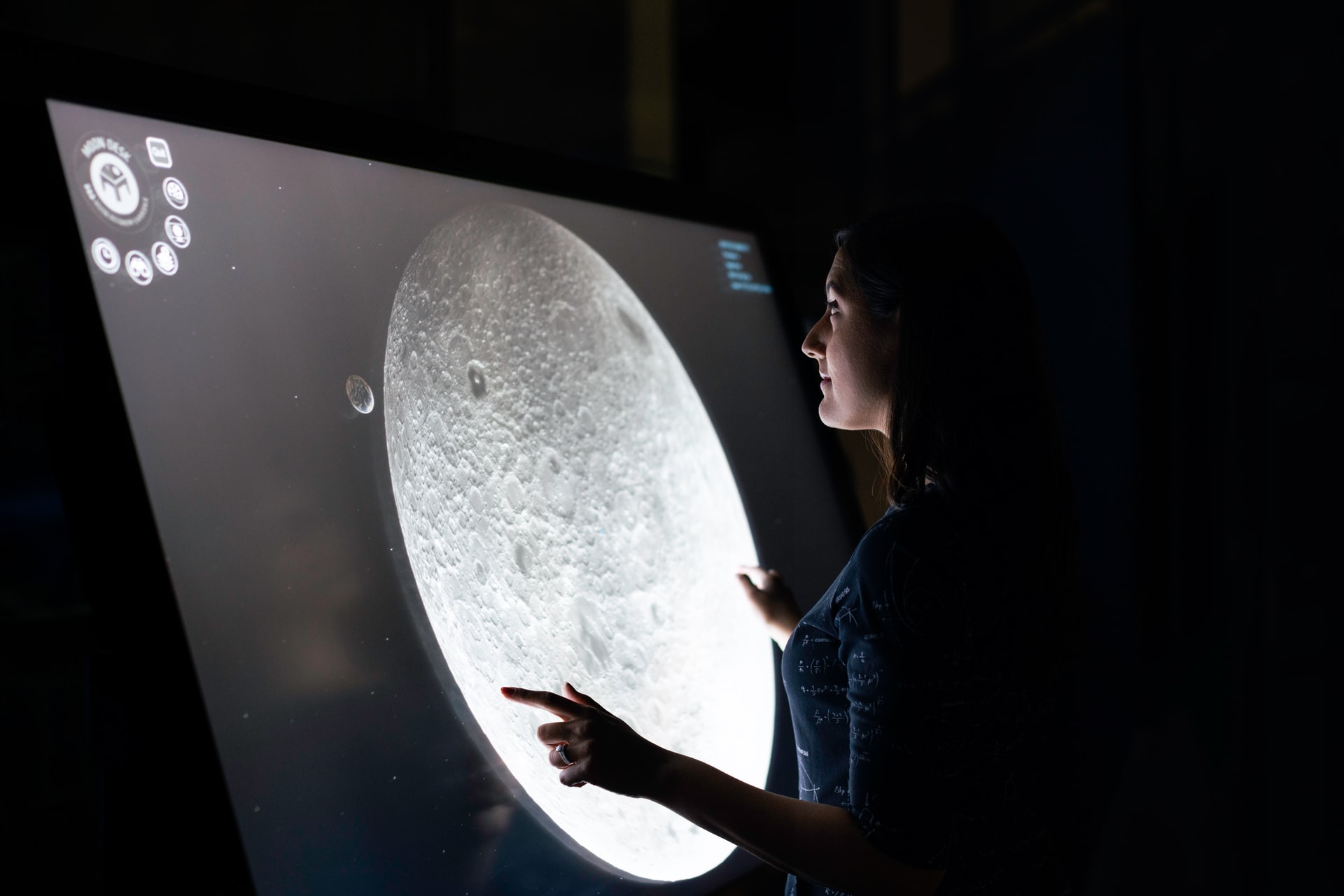 Kobieta stoi przy interaktywnej tablicy, na której wyświetlany jest księżyc.