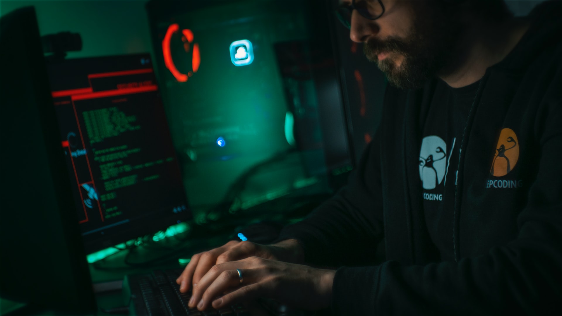 Mężczyzna siedzi przy komputerze w ciemnym otoczeniu.