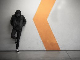 Mężczyzna w czerni stoi z opuszczoną głową oparty o ścianę na stacji metra